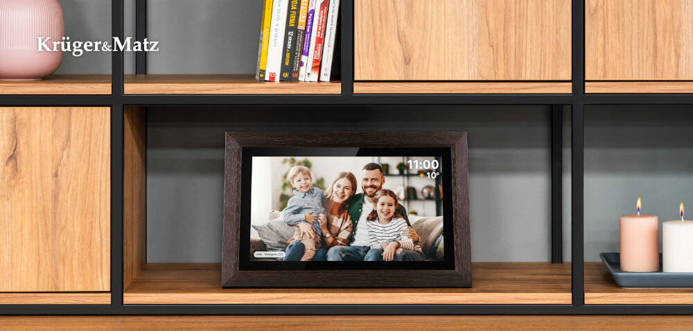 Ramka cyfrowa KRUGER&MATZ KM1102-15 Frameo 15.6 cala Brązowy prezentacja ramki ze zdjęciem i komentarzem do niej od frontu na szafce w pokoju obok świeczki książki i zielony wazon