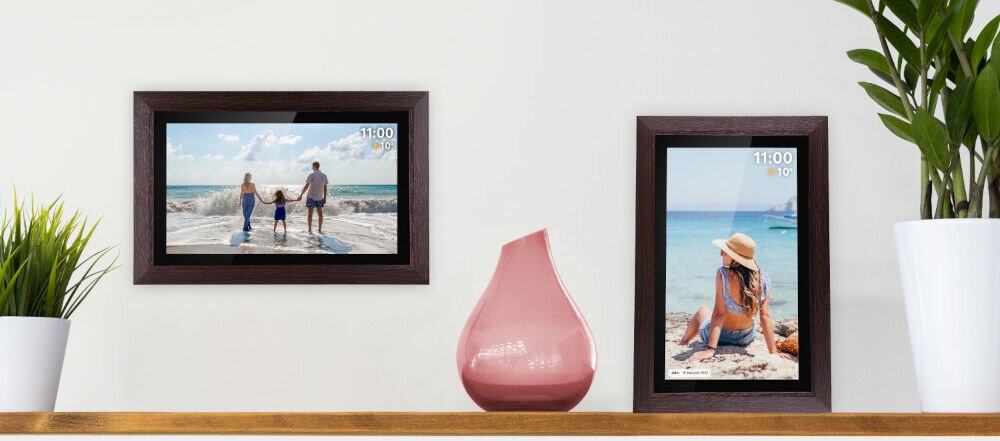 Ramka cyfrowa KRUGER&MATZ KM1102-15 Frameo 15.6 cala Brązowy prezentacja ramki ze zdjęciem w dwóch opcjach montażu wisząca poziomo i stojąca pionowo obok kwiatki pomiędzy różowy wazon jasna ściana dostosowanie odpowiedniego miejsca
