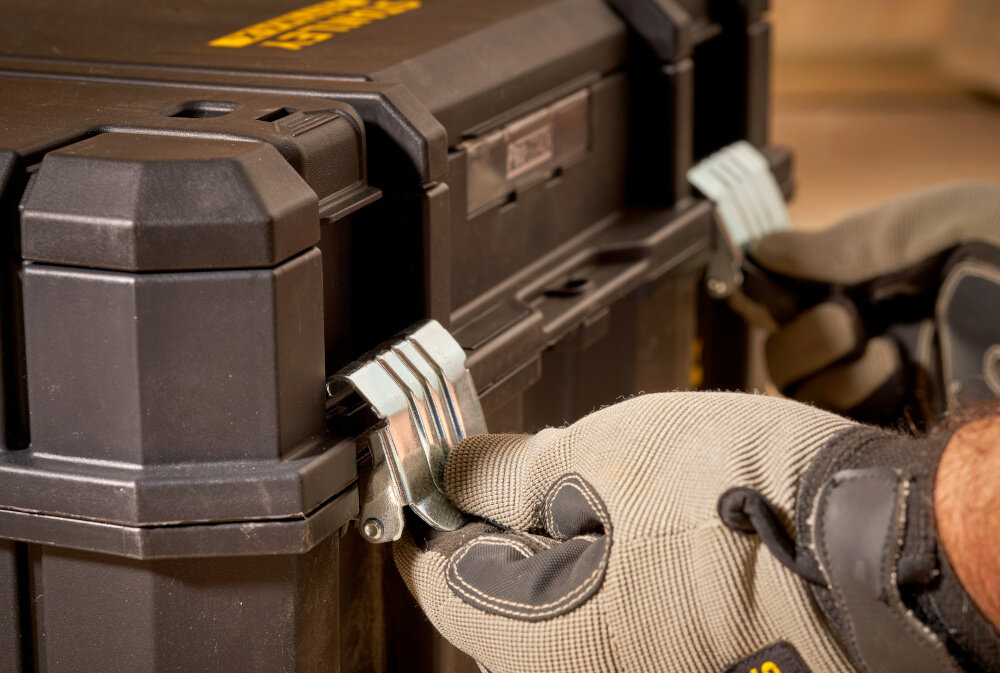 Skrzynka narzędziowa STANLEY Fatmax TSTAK FMST1-75796 zbliżenie na zamki osoba trzyma zamki w palcach dwa solidne metalowe zamki bezpieczne przechowywanie narzędzi i akcesoriów ochrona przed przypadkowym otwarciem