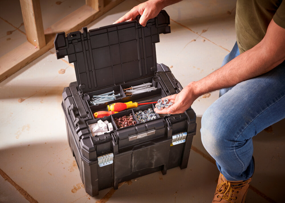 Skrzynka narzędziowa STANLEY Fatmax TSTAK FMST1-75796 skrzynka na podłodze otwarty organizer w pokrywie wypełniony akcesoriami i narzędziami osoba wyciąga z wnętrza nakrętki niewielki organizer podzielony na 7 różnych części przegródki segregacja skraca czas przygotowania do pracy ułatwia utrzymanie porządku