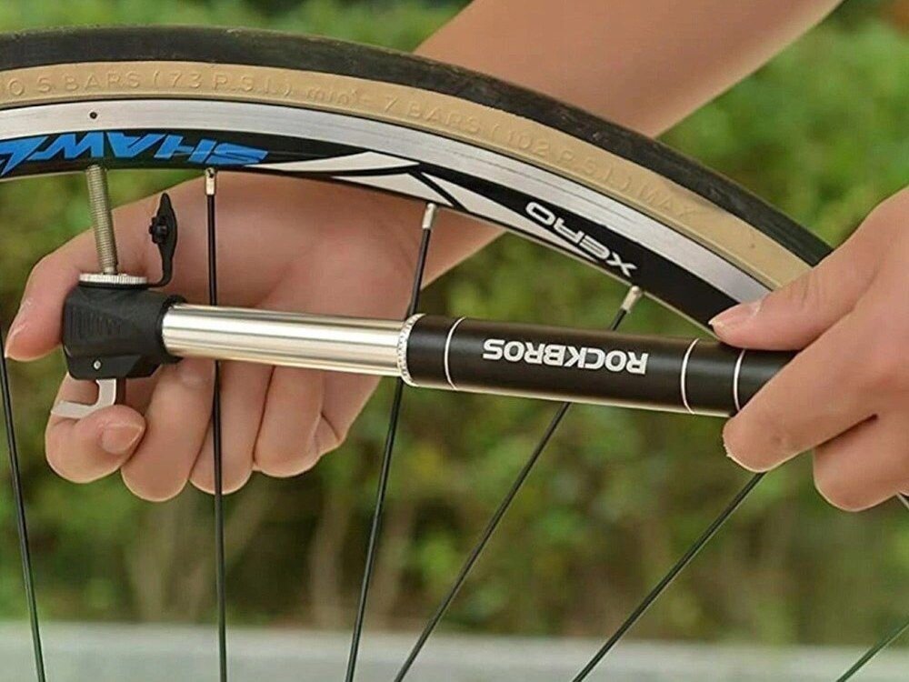 Osoba używa ręcznej pompki rowerowej do pompowania koła rowerowego. Na pompce widoczny jest napis \'ROCKBROS\'.