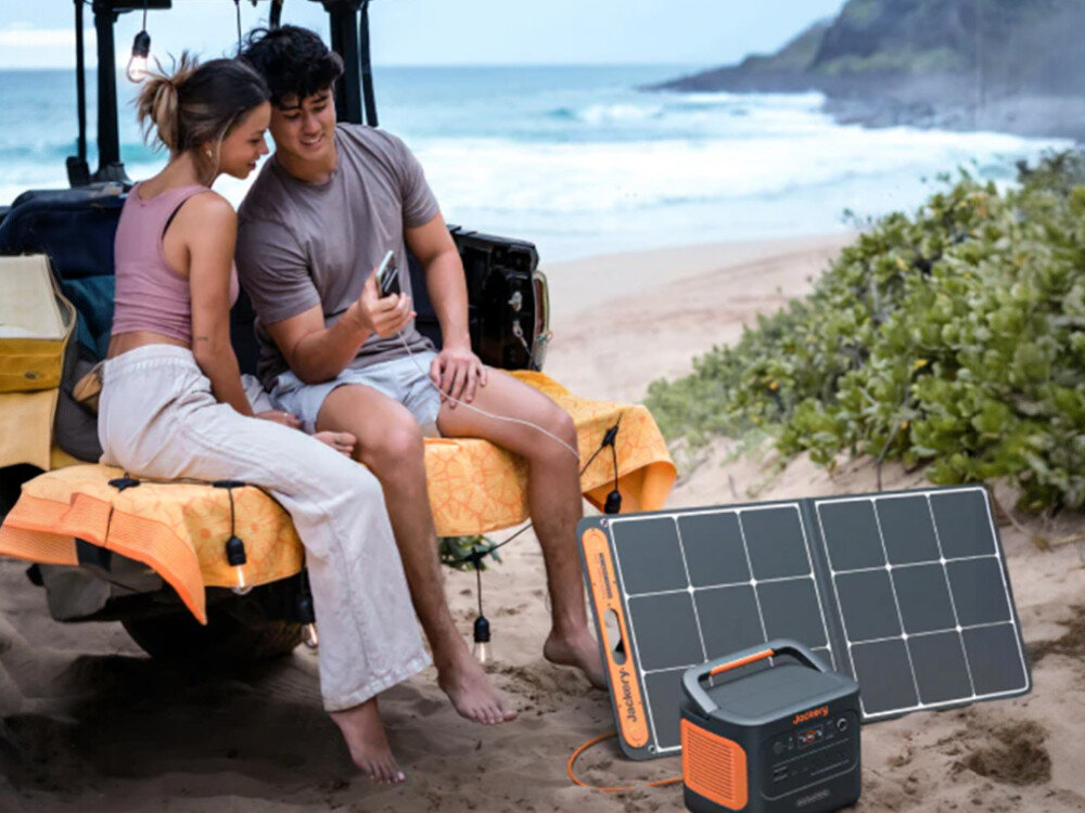 Stacja zasilania JACKERY Explorer 1000 Plus EU 1264 Wh Bank energii, para siedzi na ławce, obok stacja zasilania, teren morski