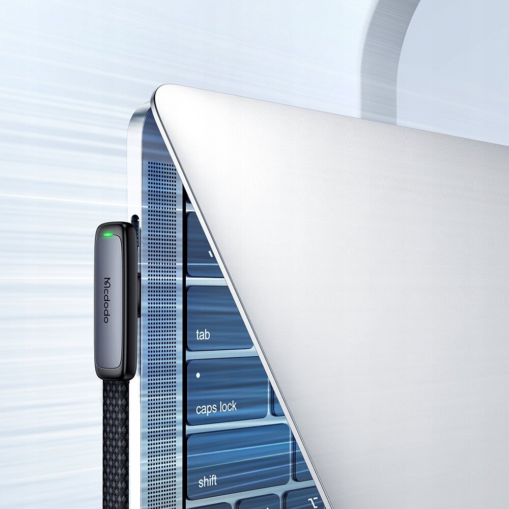 Na obrazie widoczny jest czarny kabel USB-C z logo \'Mcdodo\', podłączony do laptopa. Klawiatura laptopa pokazuje klawisze \'tab\', \'caps lock\' i \'shift\'.
