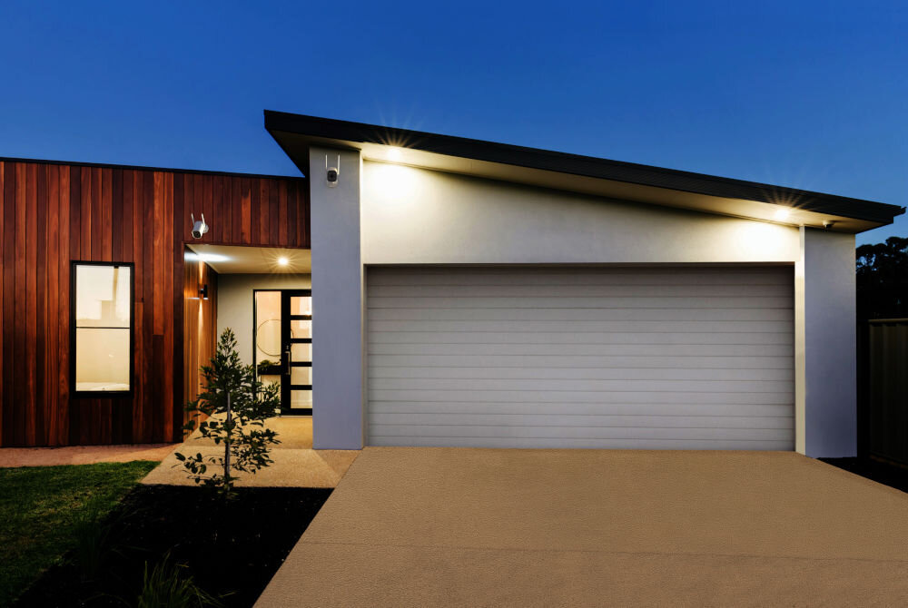 Kamera SETTI+ SC940 4MP 2K Smart, Zewnętrzna / Wewnętrzna, Wi-Fi, LAN System monitoringu domu SETTI+ SC940 – trzy białe kamery zamontowane na elewacji nowoczesnego budynku nad garażem i wejściem głównym wieczorową porą