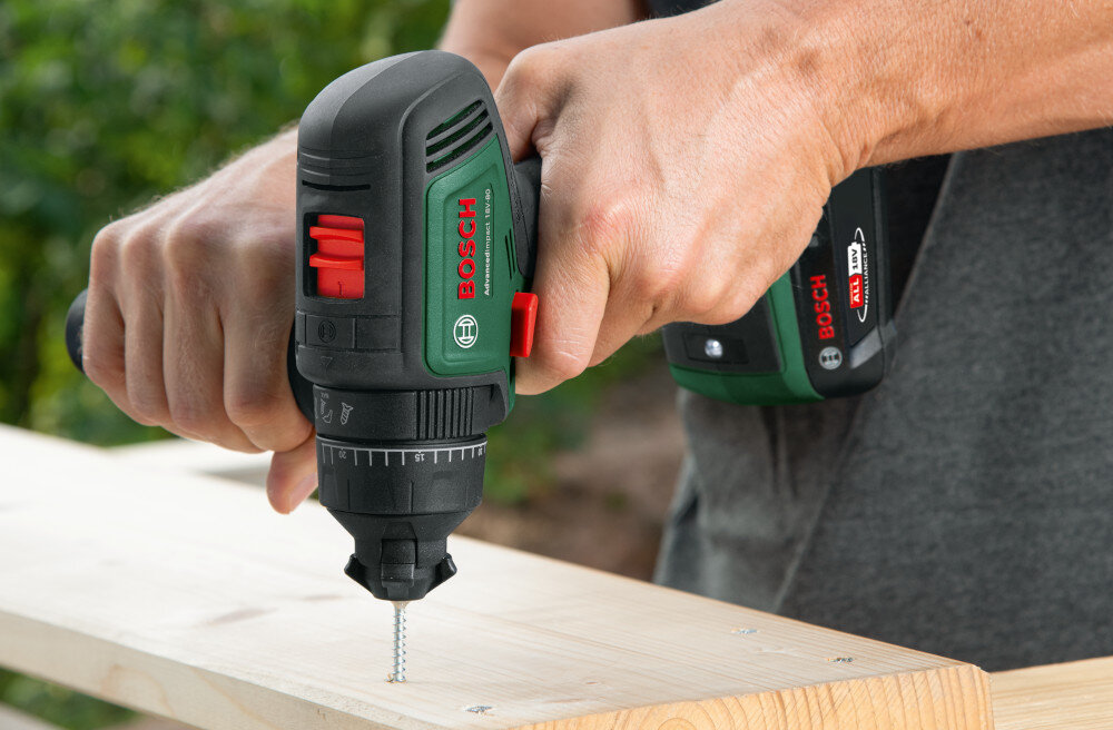 Wiertarka udarowa BOSCH AdvancedImpact 18V-80 06039E2101 ogród osoba wierci otwór w drewnianej desce widok na rękojeść dodatkową dodatkowa rękojeść stabilność narzędzia bezpieczne i precyzyjne wiercenie ergonomiczne rozmieszczenie przycisków i uchwytu