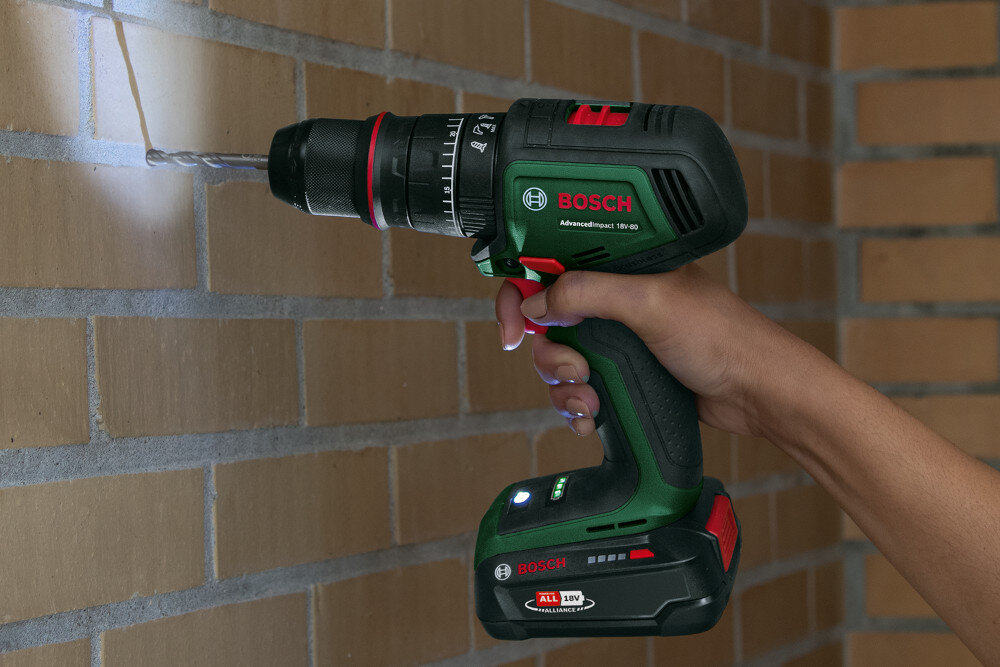 Wiertarka udarowa BOSCH AdvancedImpact 18V-80 06039E2101 ściana z cegły osoba wierci otwór w ścianie widoczne podświetlenie dioda Power LED oświetla obszar wiercenia lub wkręcania precyzyjna kontrola pozycji wiertła dokładność pracy ogranicza ryzyko błędów bezpieczne i szybkie wykonywanie zadań