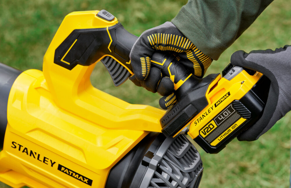 Dmuchawa do liści STANLEY SFMCBL730B-XJ akumulatorowa ogród osoba trzyma dmuchawę w dłoniach zakłada akumulator w tle trawa zasilana akumulatorem 18 V STANLEY® FATMAX® V20 pełna swoboda pracy bez kabli swoboda ruchów wielokrotne ładowanie współpracuje z innymi narzędziami z tej samej serii brak akumulatora i ładowarki w zestawie
