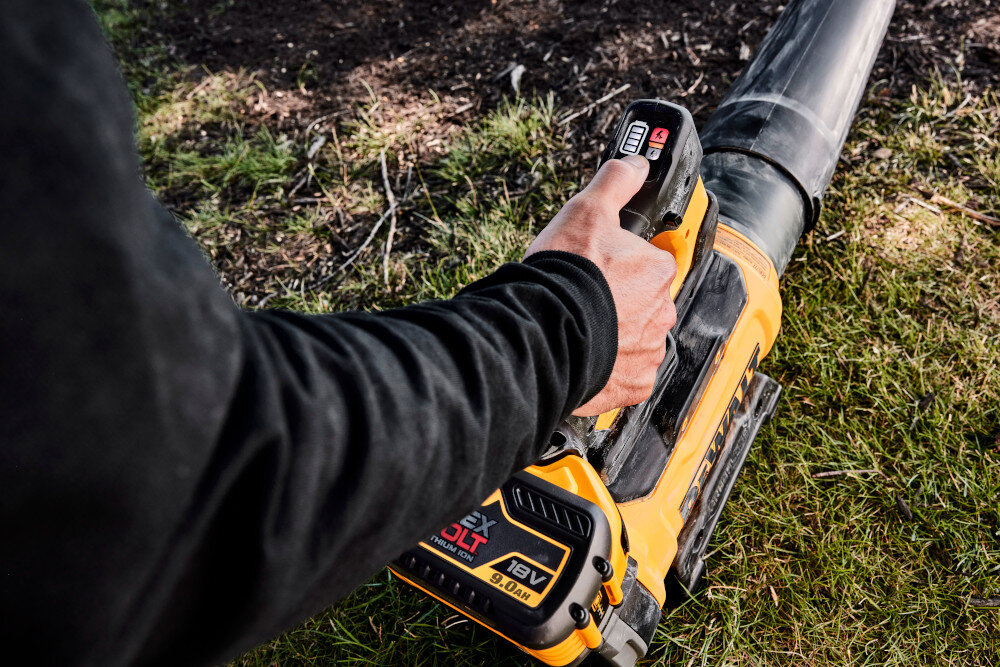 Dmuchawa do liści akumulatorowa DEWALT DCMBL777X1-QW (z akumulatorem) zbliżenie na uchwyt osoba trzyma dmuchawę w dłoni oferuje trzy ustawienia prędkości z możliwością blokady Spust z blokadą Dioda LED Poziom hałasu dmuchawy poniżej 98 dB na wszystkich trzech ustawieniach