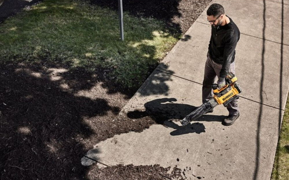 Dmuchawa do liści akumulatorowa DEWALT DCMBL777X1-QW (z akumulatorem) osoba z dmuchawą w dłoni zdmuchuje liście 3,2 kg ergonomicznie profilowanymi uchwytami paskiem na ramię dobrze wyważone komfortowe manewrowanie paskowi na ramię wygodnie noszona podczas pracy