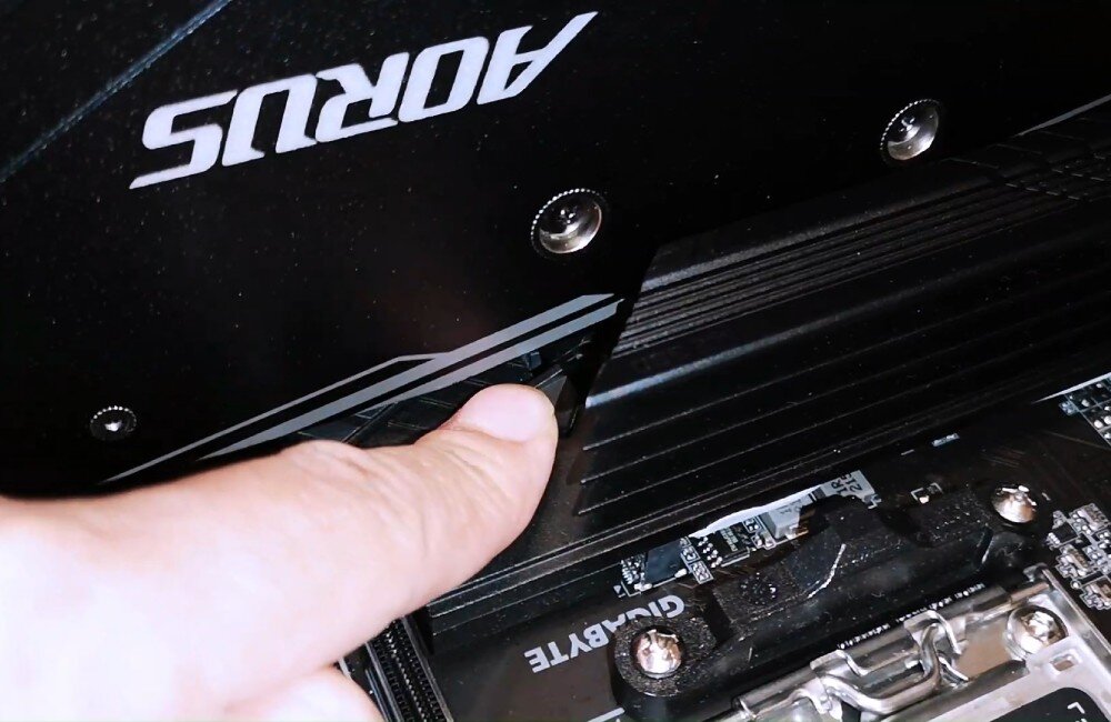 Płyta główna GIGABYTE B650 Eagle Dłoń naciskająca na plastikowy zatrzask przy slocie PCIe ułatwiający wyjęcie karty graficznej