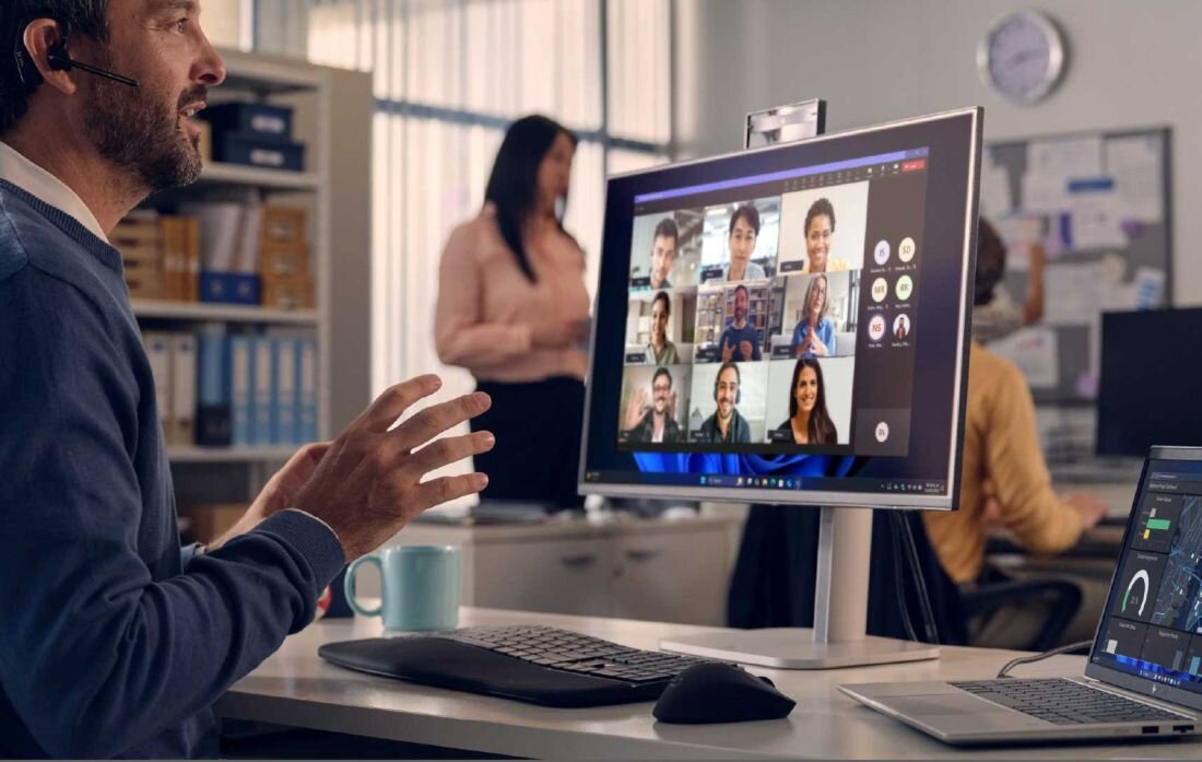 Mężczyzna w szarej bluzie gestykulujący podczas wideokonferencji na laptopie HP EliteBook 665 G11, na ekranie cztery osoby w oknach rozmowy wideo, biuro z monitorem w tle. - Dysk SSD  PCIe NVMe