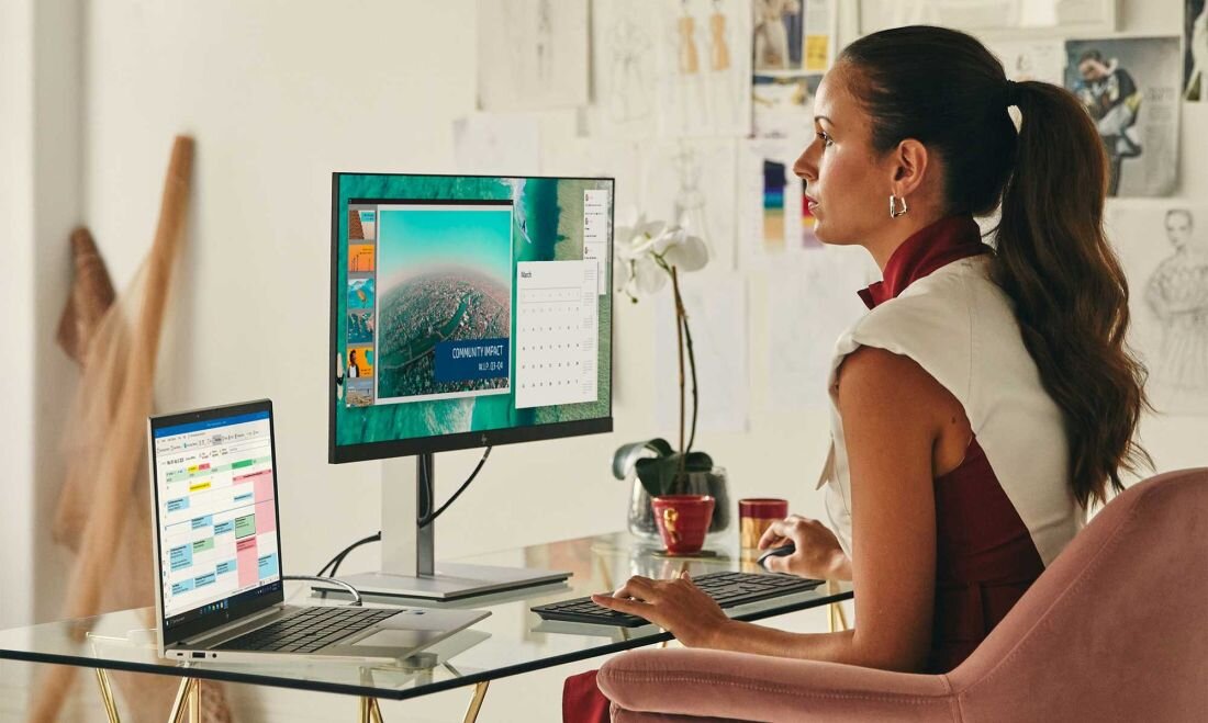 Kobieta w bordowej bluzce pracująca na laptopie HP EliteBook 665 G11 z zewnętrznym monitorem, na ekranie aplikacja do współpracy zespołowej z profilami użytkowników, stanowisko pracy z funkcją HP Sure Click. - HP Sure Click 