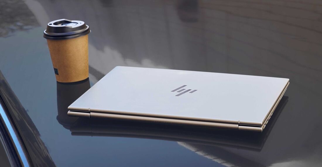 Zamknięty laptop HP EliteBook 845 w kolorze srebrnym leży na błyszczącej powierzchni obok papierowego kubka z kawą, widoczne logo HP na pokrywie, odbicie laptopa na czarnej tafli. - Opis serii EliteBook 845 G11
