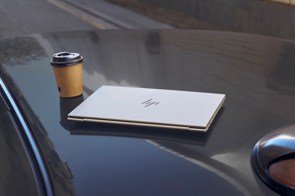 Laptop HP EliteBook 865 G11 Zamknięty laptop leży na dachu samochodu obok papierowego kubka z kawą. Logo producenta jest widoczne na pokrywie, bateria, pojemność, ładowanie