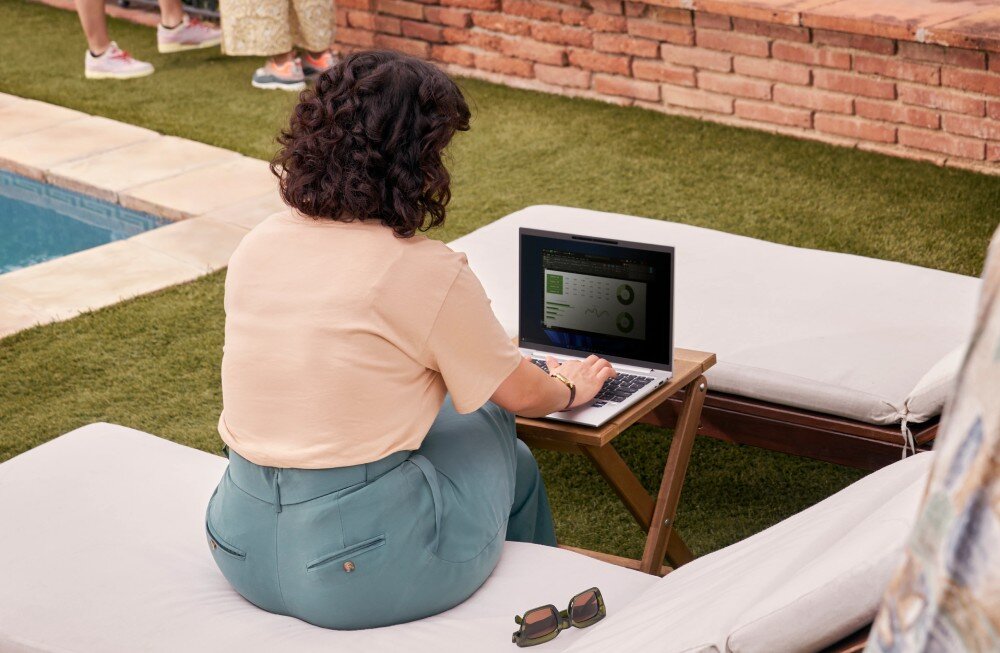 Laptop HP Elitebook 640 G11 Kobieta w jasnej bluzce i zielonych spodniach siedzi na leżaku przy basenie, pracując na laptopie. Urządzenie stoi na małym drewnianym stoliku, a obok na leżaku leżą okulary przeciwsłoneczne, cechy, ekran, przekątna, rozdzielczość, matryca, ramka