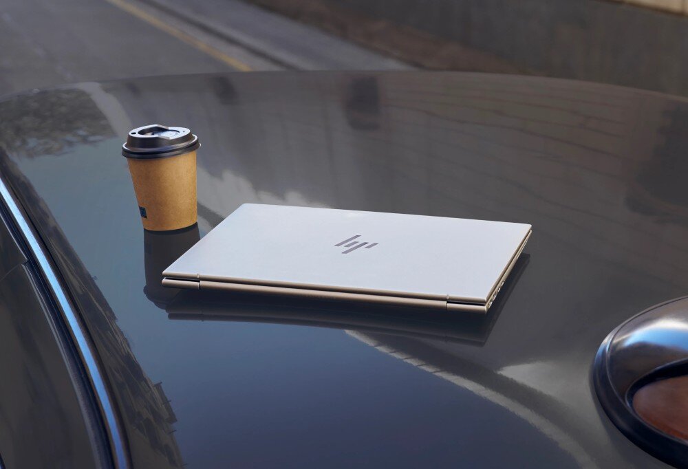 Laptop HP EliteBook 1040 G11 Laptop leżący na dachu samochodu, obok stojący papierowy kubek z kawą, bateria, zasilanie, ładowanie