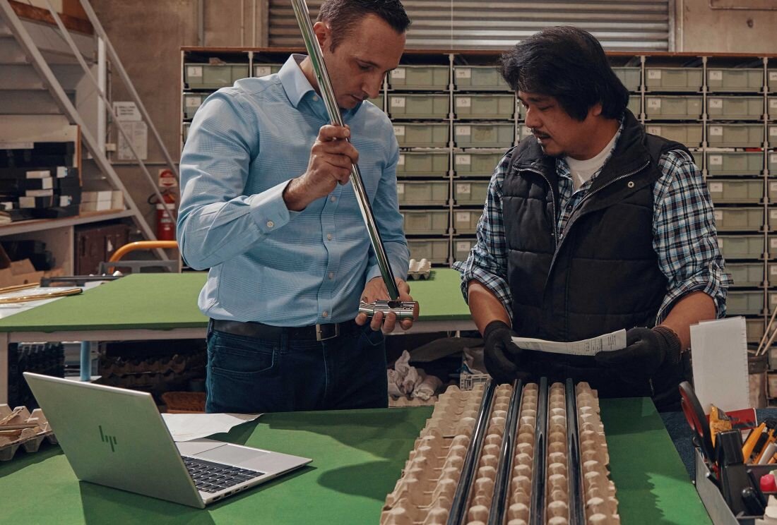 Dwóch pracowników w magazynie używających laptopa HP EliteBook 660 G11 do kontroli jakości, mężczyzna w niebieskiej koszuli trzyma długi przyrząd pomiarowy, drugi w kamizelce sprawdza dokumenty, na stole kartony z jajkami. - Pamięć DDR5