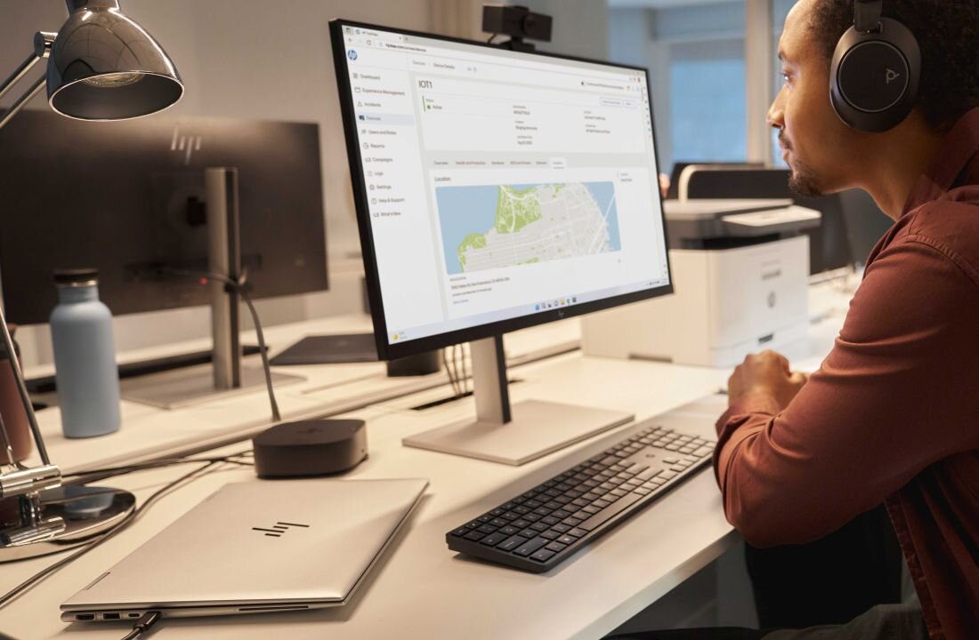 Laptop HP EliteBook 830 - Mężczyzna w słuchawkach siedzi przy biurku z komputerem i monitorem, obok laptop HP EliteBook 830. zintegrowana grafika Intel Graphics.  