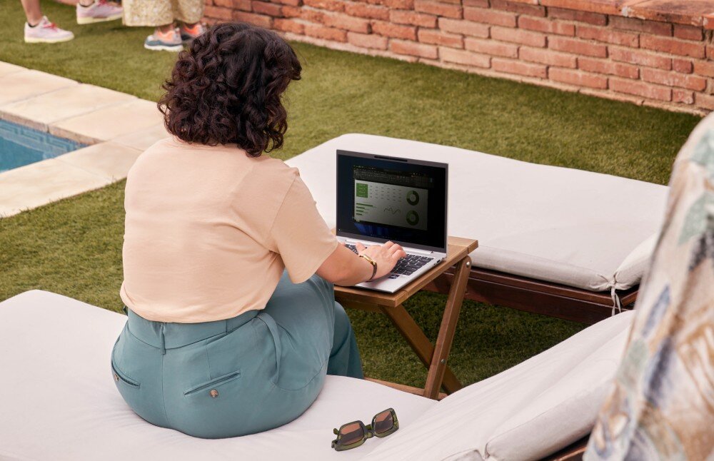 Laptop HP EliteBook 1040 G11 Kobieta siedząca na leżaku na zewnątrz, pracująca na laptopie. Obok okulary przeciwsłoneczne, a w tle zielona trawa i ceglana ściana, dysk, pojemność, interfejs