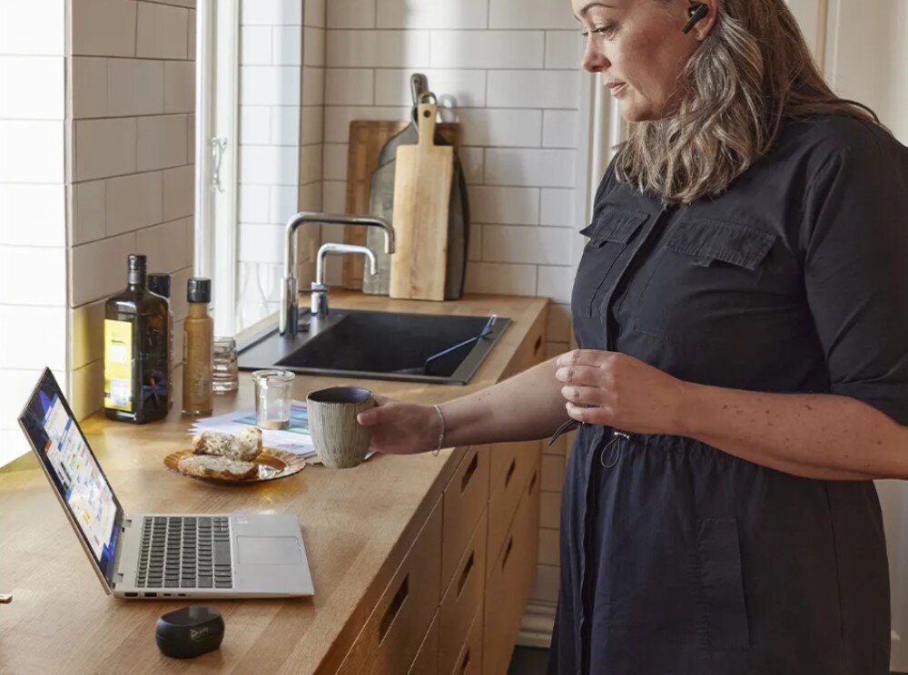 Laptop HP EliteBook 865 G11 Kobieta w ciemnej sukience stoi w kuchni, trzyma kubek i patrzy na ekran laptopa ustawionego na drewnianym blacie, klawiatura, podświetlenie, blok numeryczny, touchpad, kolor