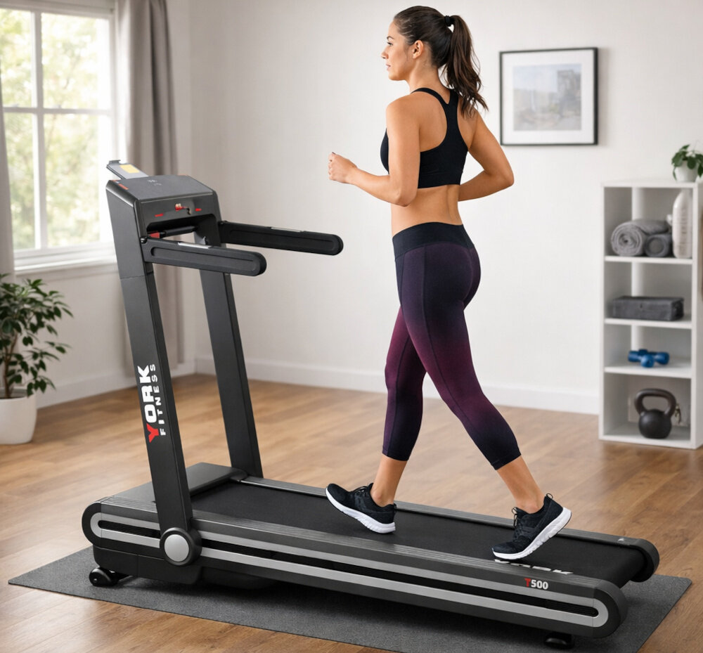 Bieżnia elektryczna YORK FITNESS T500 1470W 16 km-h dom pokój osoba w czarnym stroju sportowym biegnie na bieżni w tle regał z przyrządami do ćwiczeń okno drewniana podłoga trening w domu wszechstronne zastosowanie kondycja zdrowie trening cardio