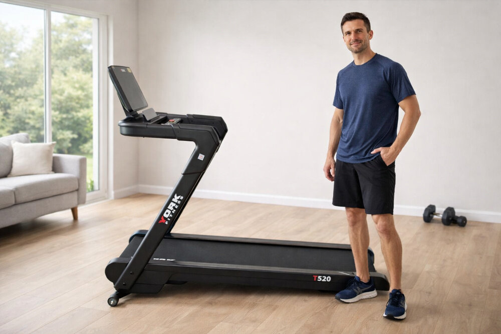 Bieżnia elektryczna YORK FITNESS T520 1839W 20 km-h dom pokój osoba w stroju sportowym stoi obok bieżni w tle okno drewniana podłoga trening w domu wszechstronne zastosowanie kondycja zdrowie trening cardio