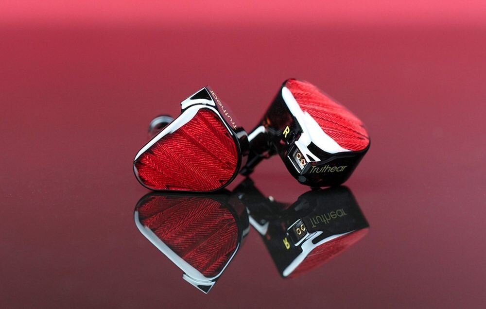Słuchawki dokanałowe TRUTHEAR Zero, przetwornik 10 mm, przetwornik 7,8 mm CCAW, bas, wokale i detale, Czerwone słuchawki TRUTHEAR Zero Red leżące na błyszczącej, czerwonej powierzchni z widocznymi gniazdami 2-pin i oznaczeniem kanału