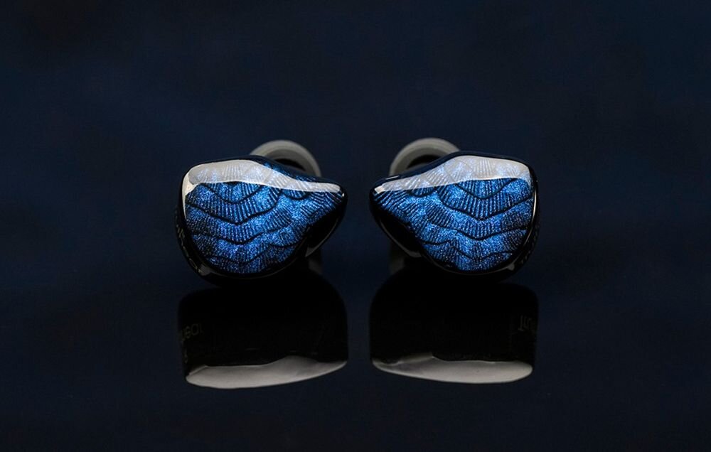 Słuchawki dokanałowe TRUTHEAR Nova, pasmo 8 Hz–40 kHz, efektywny zakres 20 Hz–20 kHz, szczegóły nagrań, Dwie obudowy słuchawek TRUTHEAR Nova z mieniącym się, niebieskim wzorem ułożone na czarnym, lustrzanym tle