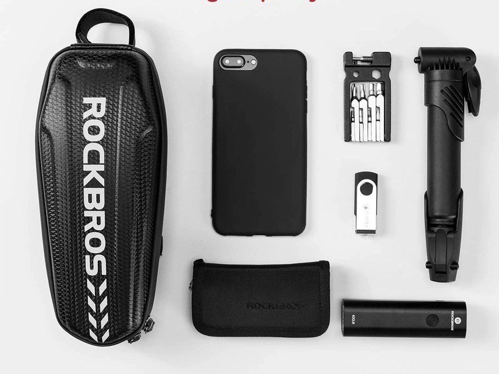 Na obrazie znajduje się czarna torba rowerowa z napisem \'ROCKBROS\', obok której leżą czarny futerał na telefon, zestaw narzędzi, pompka, pendrive, etui oraz latarka. Wszystkie przedmioty są ułożone na jasnym tle.