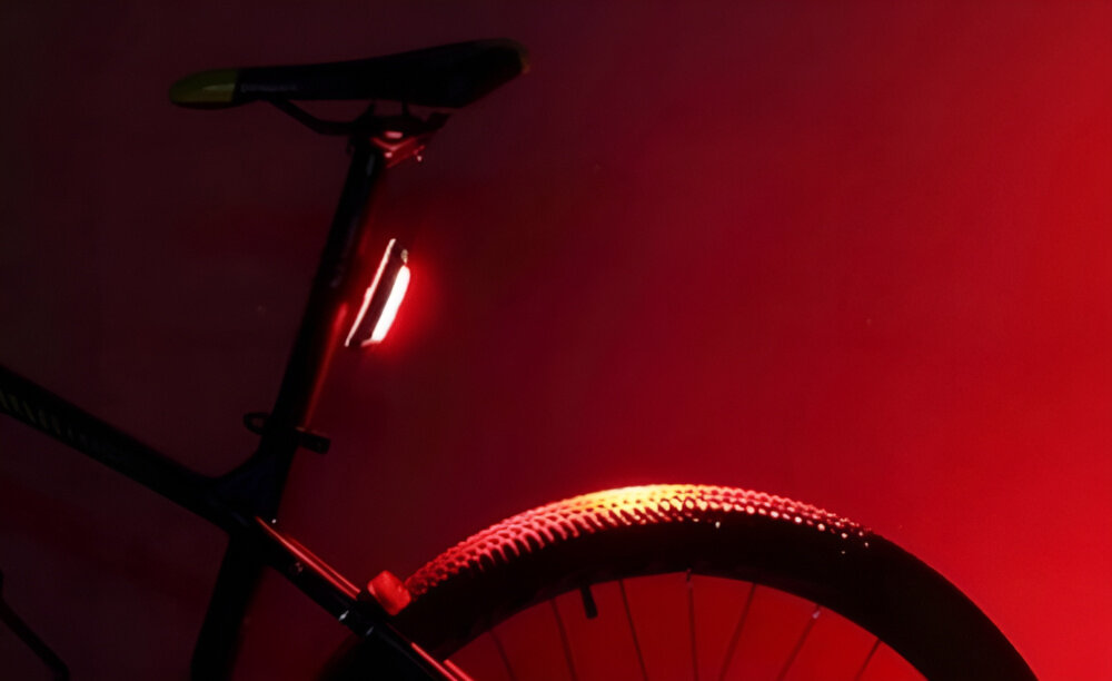 Lampka rowerowa ROCKBROS A54BK czerwone tło lampka umieszczona pod siodełkiem widok z boku pięć różnych trybów świecenia dostosowanie natężenia i częstotliwości światła do warunków na zewnątrz stałe światło migające tryby tryby o niższej intensywności pozwalają oszczędzać baterię podczas dłuższych tras