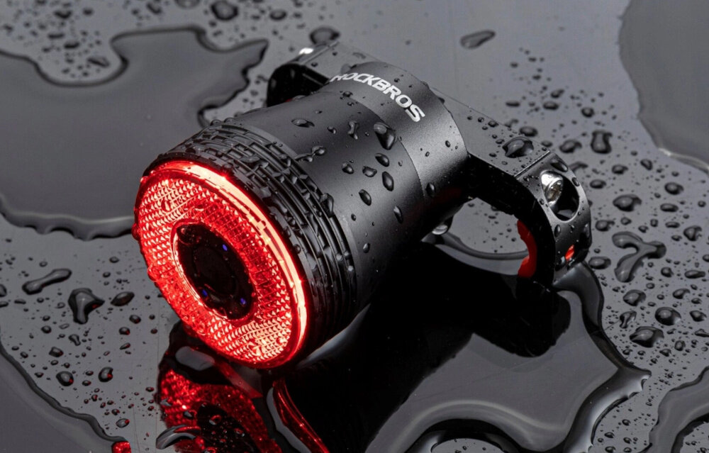 Lampka rowerowa ROCKBROS Q5 157347 droga lampka leży na drodze jest mokra krople wody bezpieczeństwo wygoda widoczność