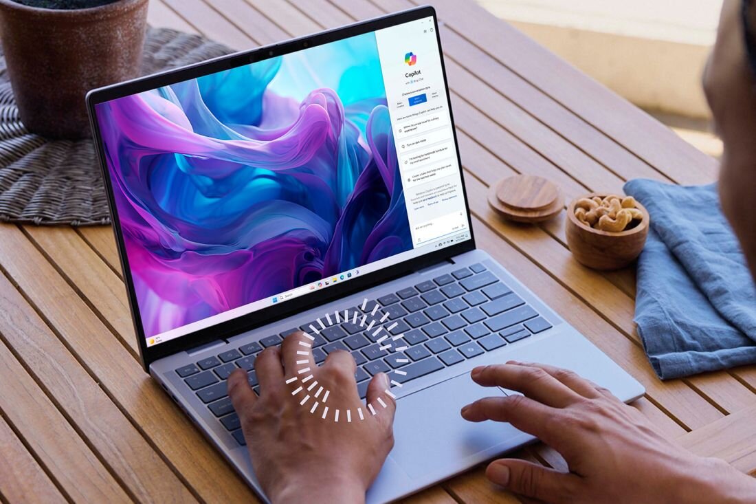 Osoba pracująca na laptopie Dell Inspiron 14 Plus 7441 na drewnianym stole, ekran z kolorową grafiką i otwartą aplikacją Copilot, obok miseczki z orzechami i serwetka. - Copilot 