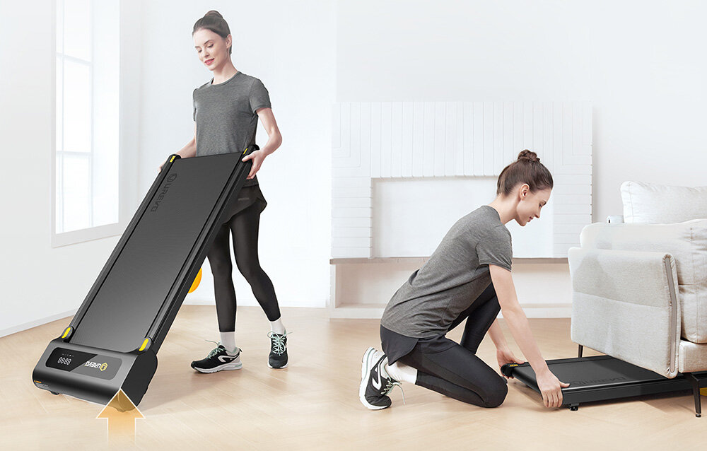 Bieżnia elektryczna UREVO Spacewalk SP1 Lite 1677W 6km-h pokój jedna osoba przestawia bieżnię a druga chowa bieżnię pod kanapę w tle jasna ściana 12,4 cm wysokości wymiary 126,5 × 53 x 12,4 cm sprzęt nie dominuje przestrzeni praktyczne kółka transportowe