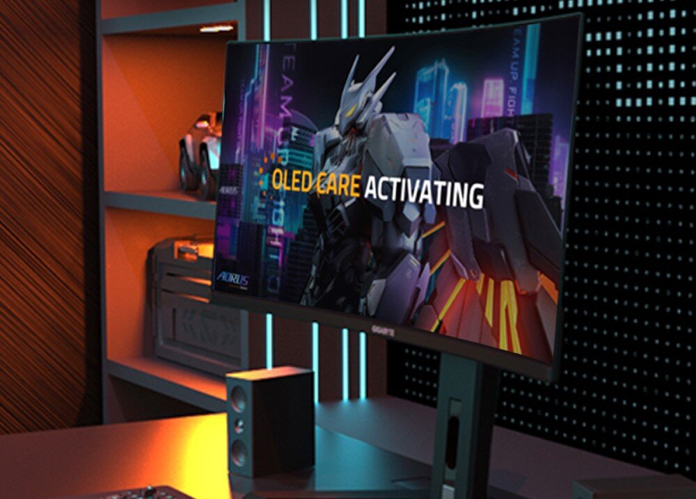 Monitor GIGABYTE MO34WQC Monitor stojący na biurku w pokoju gracza z napisem 'OLED CARE ACTIVATING' i grafiką robota, ochrona ekranu, wypalenie
