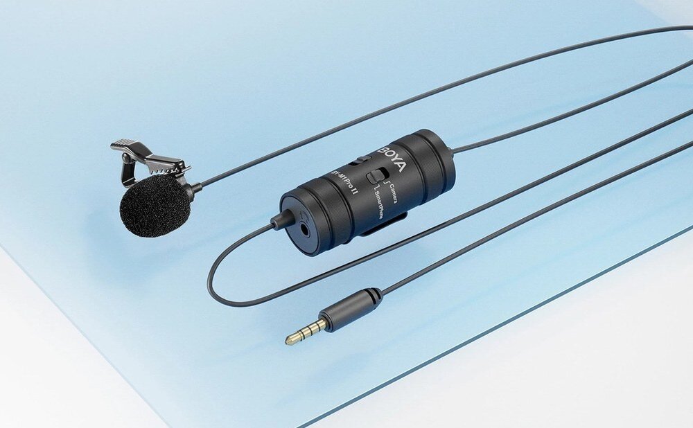 Mikrofon BOYA BY-M1 Pro II Czarny mikrofon krawatowy BOYA BY-M1 Pro II z klipsem, modułem i kablem zakończonym złotą wtyczką 3,5 mm, na niebieskim tle, obudowa, złącze, klips