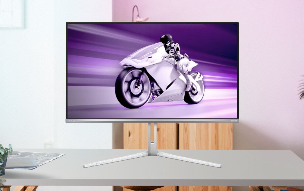 Monitor PHILIPS Evnia 32M2N8900 Monitor na biurku w jasnym pomieszczeniu, wyświetlający dynamiczny obraz motocyklisty w fioletowej tonacji, kolory, odwzorowanie barw, głębia