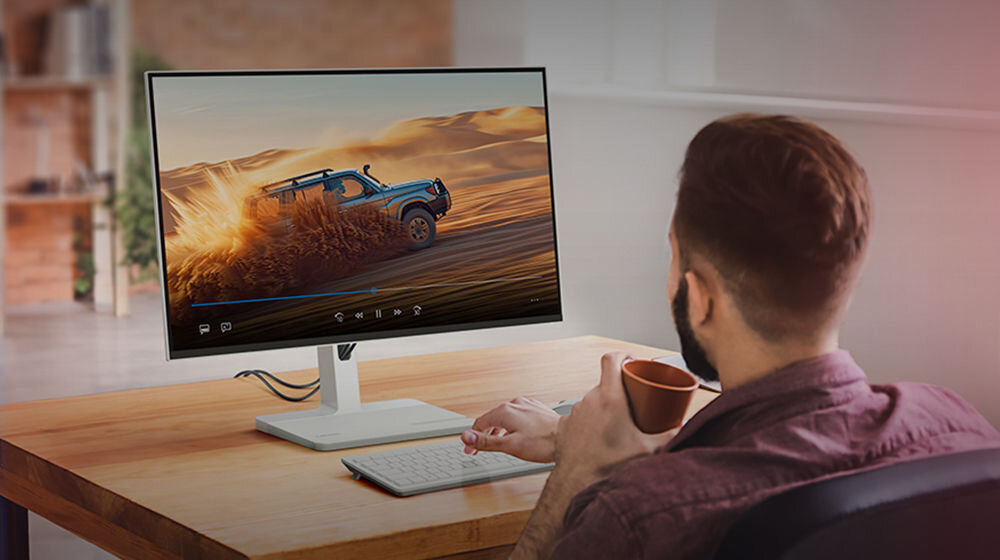 Monitor LENOVO L27q-4A 27 cali 2560x1440px IPS 100Hz 1 ms [MPRT] prezentacja monitora podczas oglądania filmiku na nim mężczyzna siedzący przy biurku i trzymający kubek odświeżanie 100 Hz płynny stabilny komfort