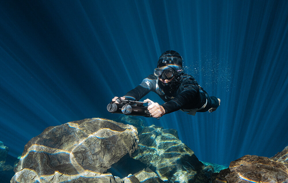 Skuter podwodny WAYDOO Subnado Czarny + zestaw startowy osoba w piance w głębinach wody w dłoni trzyma skuter płynie waga 1,4 kg wymiary 38 x 6 cm pojemność akumulatora wynosi 98 Wh możesz bezpiecznie przewozić również w samolocie