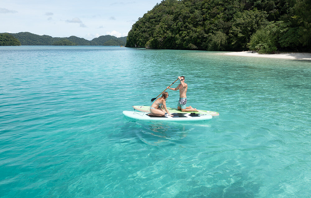Skuter podwodny WAYDOO Subnado Czarny + zestaw dla SUP woda plaża dwie osoby na supach pływają po wodzie w tle drzewa lekka i niewielka konstrukcja intuicyjna obsługa dla dorosłych i dzieci 3 poziomy prędkości szybkie ładowanie funkcja powerbanku specjalne mocowanie umożliwia montaż pod deską SUP