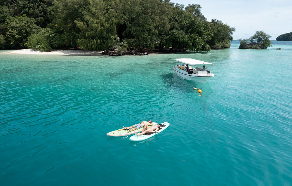 Skuter podwodny WAYDOO Subnado Czarny + zestaw dla SUP woda plaża dwie osoby na supach pływają po wodzie w tle drzewa łódka technologia opracowana przez WAYDOO czas ładowania około 1,2 godziny czas pracy nawet do 56 minut powerbank z mocą do 100 W