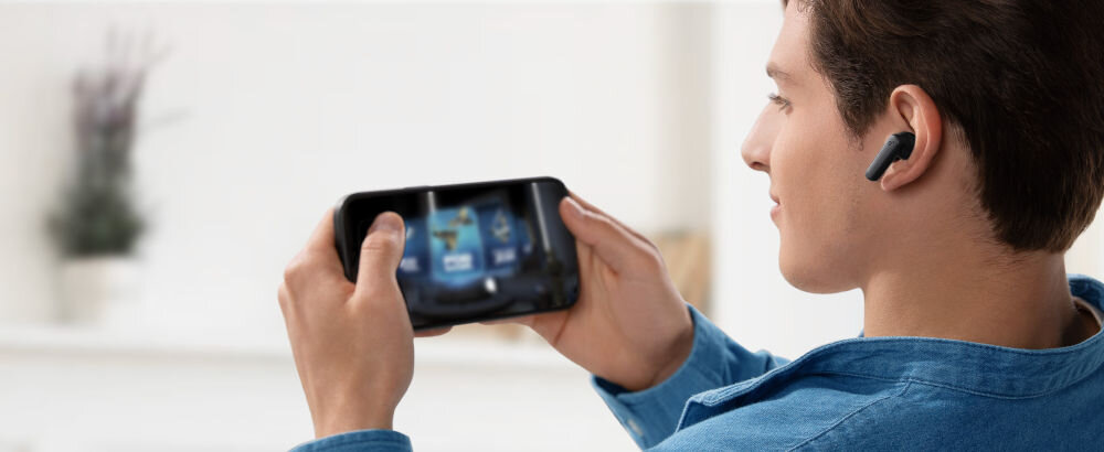 Słuchawki dokanałowe SOUNDCORE R50i v2 tryb gry aplikacja ulepszone efekty dźwiękowe gaming, osoba z założonymi słuchawkami dokanałowymi trzymająca smartfon w rękach