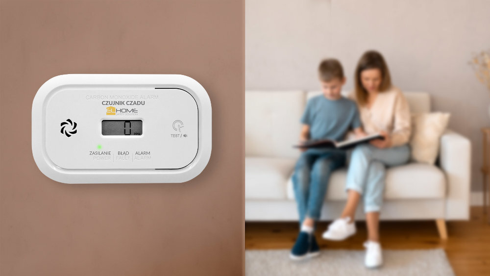 Czujnik tlenku węgla EL HOME CD-17A2v2300 czujnik powieszony na scianie, w tle rodzica czytająca książkę