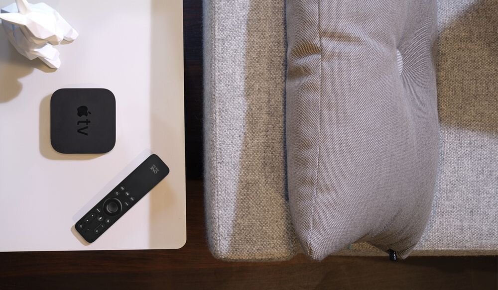 ONE FOR ALL URC1110 pilot do Apple TV obsługa 3 urządzeń podświetlenie ruchowe, Podświetlany pilot - zamiennik do Apple TV One For All URC1110 leżący na białym stoliku przy kanapie