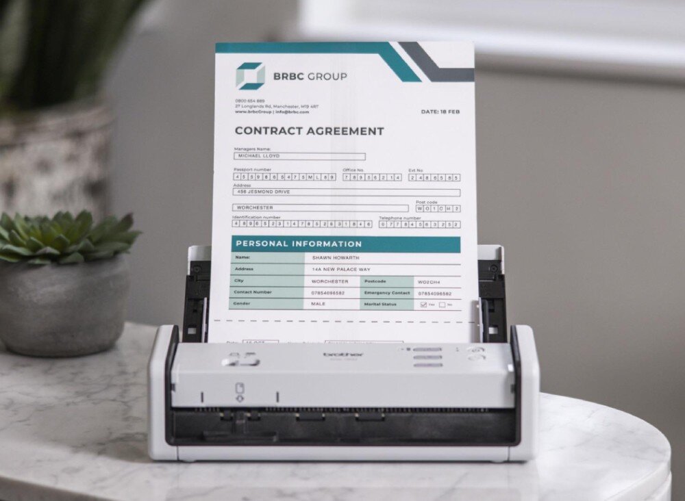 Skaner BROTHER ADS-1300 Skaner umieszczony na marmurowym blacie z arkuszem papieru w trakcie skanowania. Dokument zawiera dane osobowe, działanie, podłączenie, prędkość, formaty