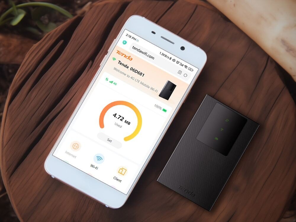 Router TENDA 4G180 v4.0 Biały smartfon leżący na drewnianej powierzchni obok czarnego rutera, wyświetlający interfejs aplikacji do zarządzania siecią z logo Tenda i licznikiem zużycia danych