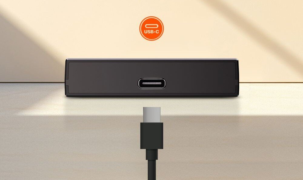 Router TENDA 4G180 v4.0 Zbliżenie na dolną krawędź czarnego urządzenia z centralnie umieszczonym portem USB-C, do którego z dołu zbliża się pasująca wtyczka kabla, z pomarańczową ikoną 'USB-C' powyżej