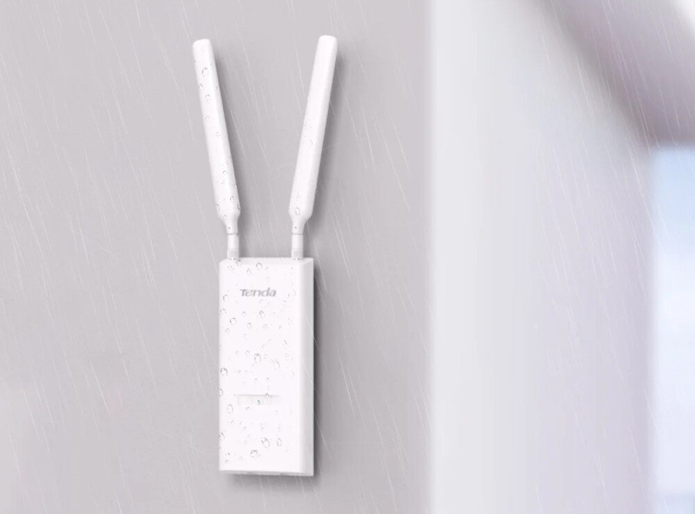 Na obrazie widoczny jest biały punkt dostępu z dwiema antenami, zamontowany na ścianie, pokryty kroplami wody. Na urządzeniu znajduje się logo \'Tenda\'.
