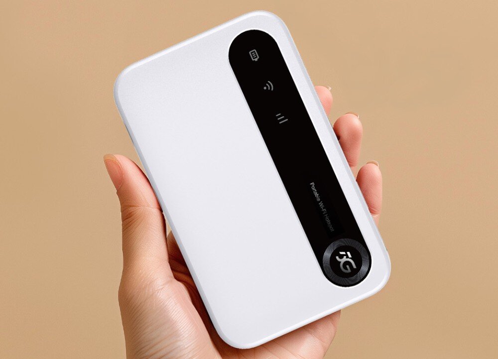 Router ZTE U50 2.4 / 5 GHz (DualBand), Gniazdo SIM Mobilny router trzymany w dłoni, ma kompaktową białą obudowę z czarnym panelem na górze, gdzie znajdują się ikony statusu sieci, Wi-Fi i baterii, opis