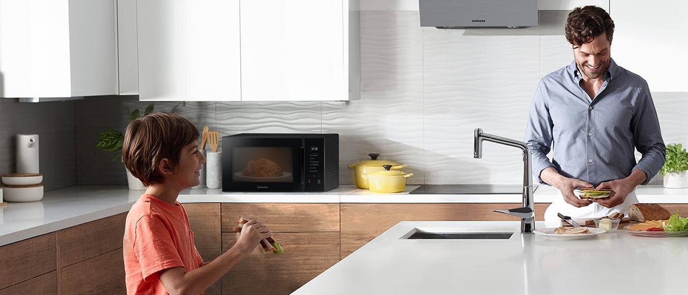 Zdjęcie ojca i syna przyrządzających wspólny posiłek w kuchni pokazuje wygodę użytkowania kuchenki mikrofalowej Samsung MG30T5018CK dostępnej w sklepach Media Expert