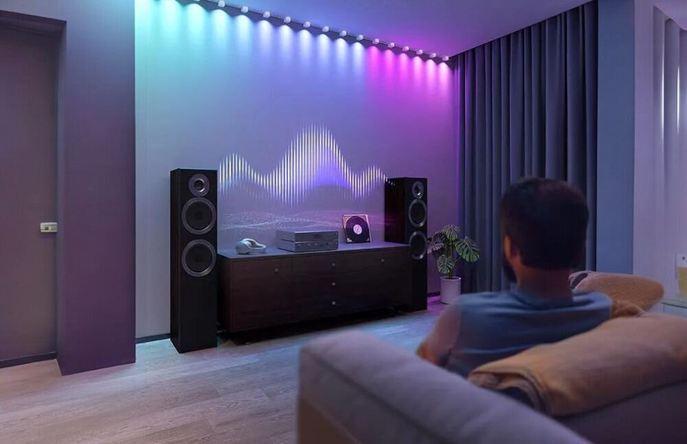 Taśma LED GOVEE H608B 3 m String Downlights Wi-Fi/Bluetooth, kolory, 15 punktów, efekty, ścienne, osoba siedzi na sofie w pokoju oświetlanym taśmą LED goove przy muzyce